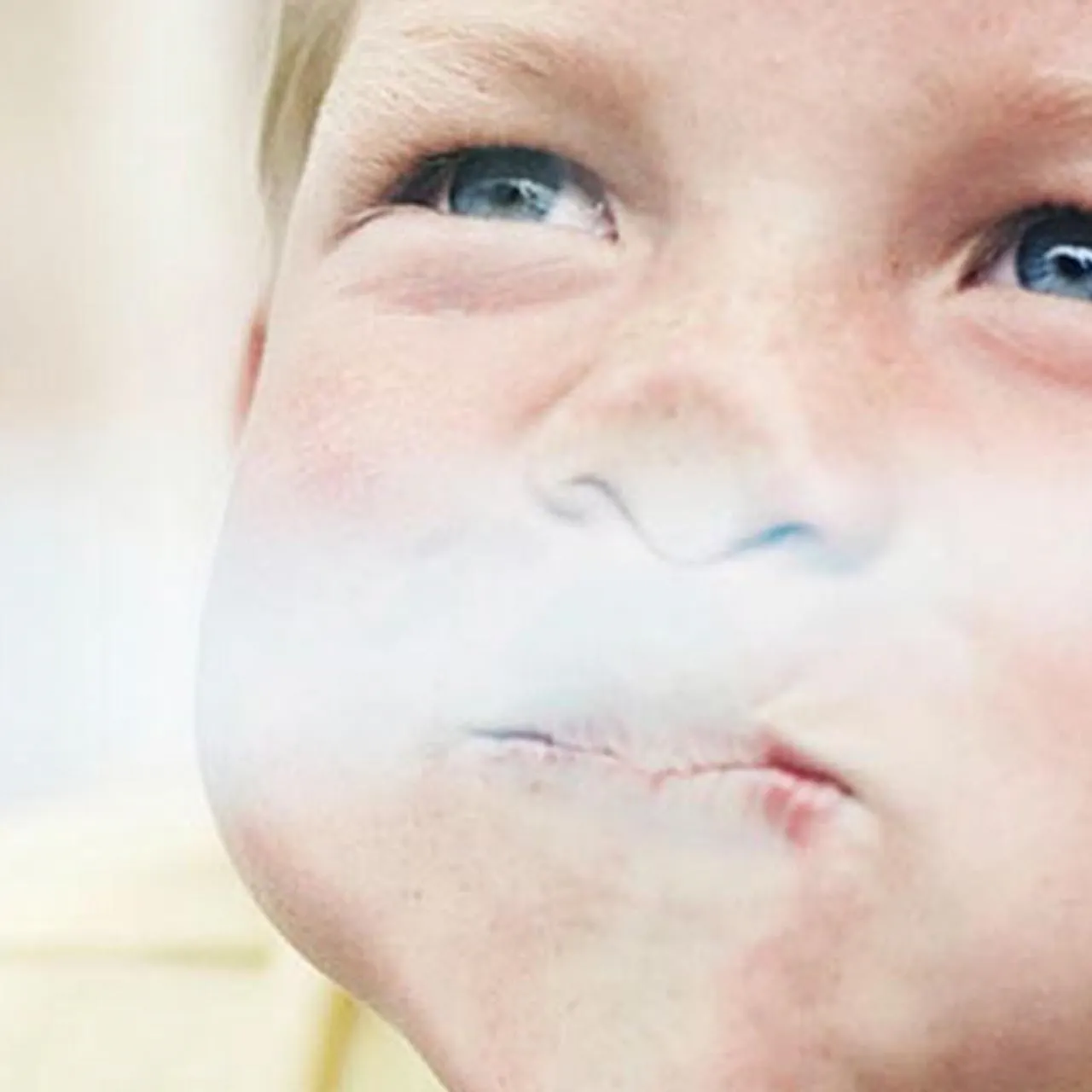 A playful close-up of a child puffing his cheeks against a Velux window and looking upwards 